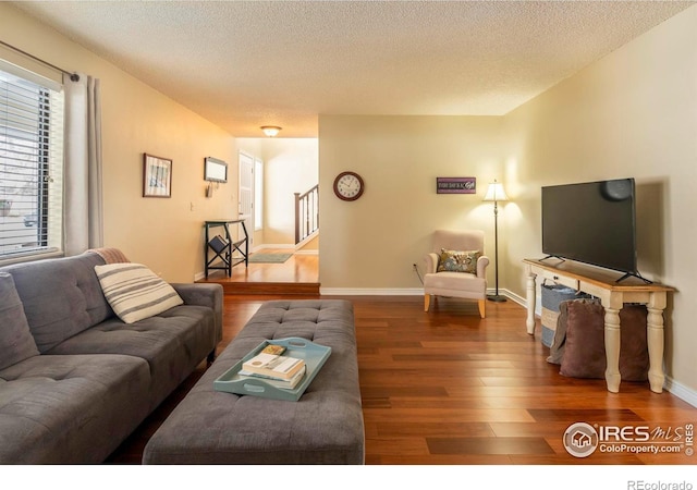 living area with stairs, a textured ceiling, wood finished floors, and baseboards