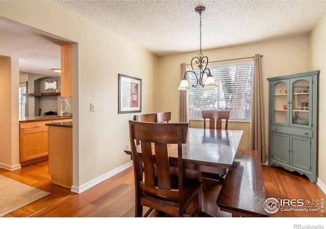 dining area with a textured ceiling, light wood-type flooring, an inviting chandelier, and baseboards