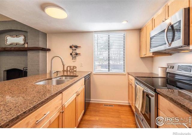 kitchen featuring visible vents, dark stone counters, stainless steel appliances, a brick fireplace, and a sink