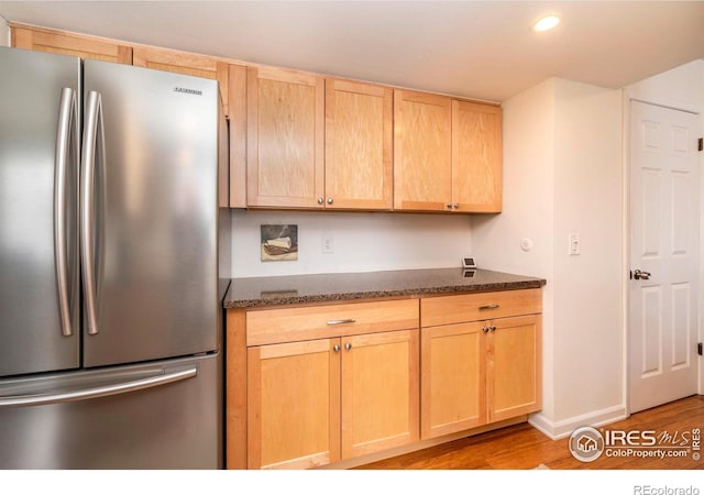 kitchen with dark stone countertops, light brown cabinets, and freestanding refrigerator