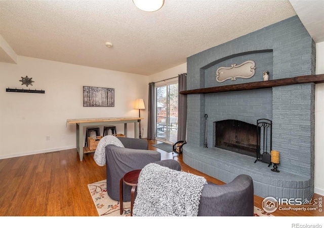 living room with a fireplace, a textured ceiling, baseboards, and wood finished floors