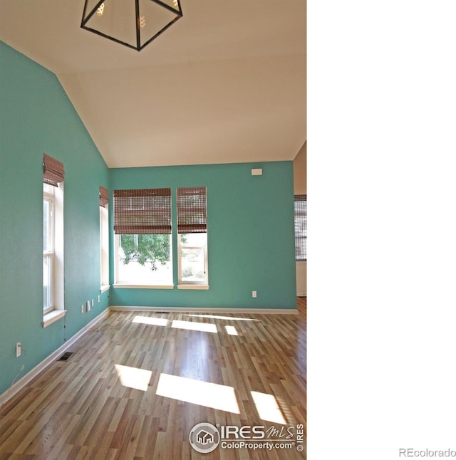 spare room featuring light wood-style floors, lofted ceiling, visible vents, and baseboards