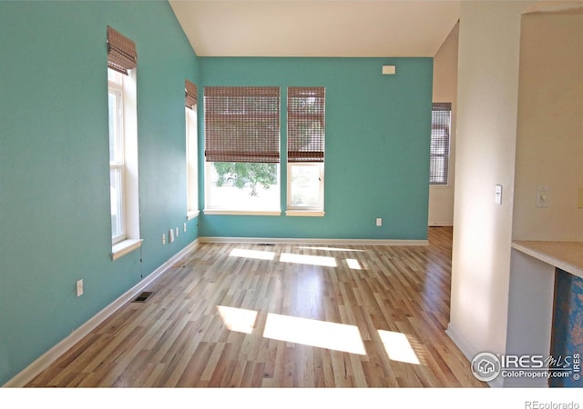 spare room featuring light wood-style floors, lofted ceiling, visible vents, and baseboards