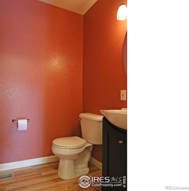 half bathroom featuring visible vents, toilet, vanity, wood finished floors, and baseboards