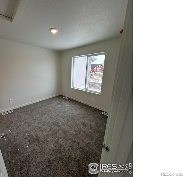 spare room featuring baseboards, visible vents, and dark colored carpet