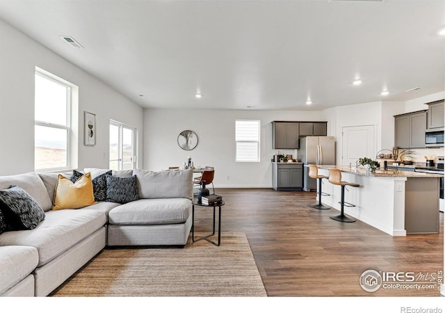 living room featuring dark wood-type flooring, recessed lighting, visible vents, and a healthy amount of sunlight