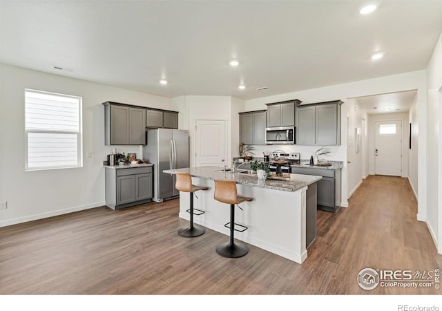 kitchen with stainless steel appliances, a breakfast bar, gray cabinets, and an island with sink