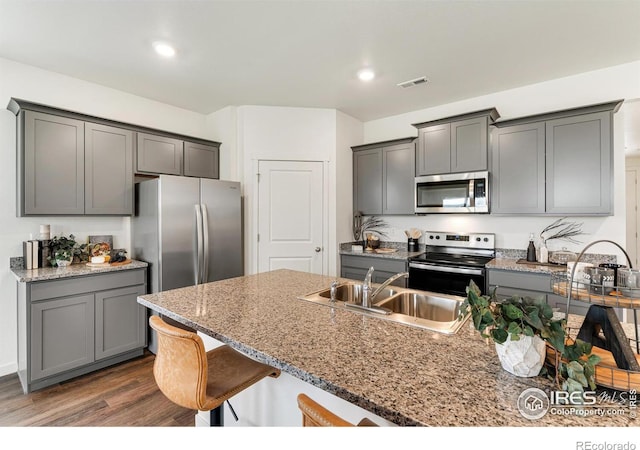 kitchen featuring dark wood-style floors, stainless steel appliances, gray cabinetry, a sink, and light stone countertops