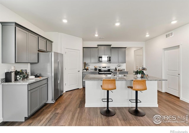 kitchen with stainless steel appliances, gray cabinets, a kitchen island with sink, and dark wood finished floors