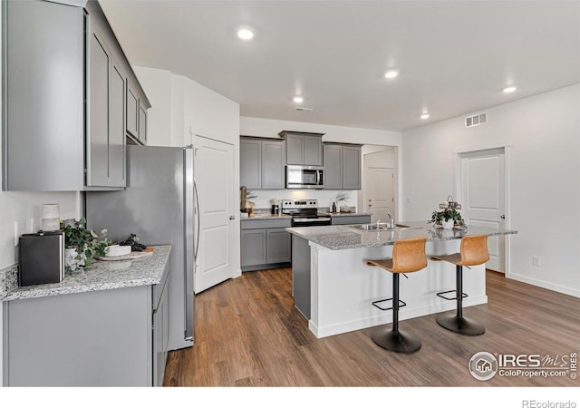 kitchen with a center island with sink, gray cabinets, visible vents, appliances with stainless steel finishes, and light stone countertops