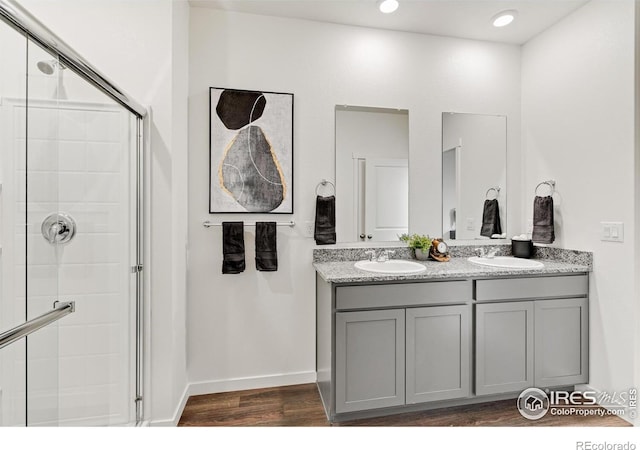 bathroom featuring double vanity, wood finished floors, a stall shower, and a sink