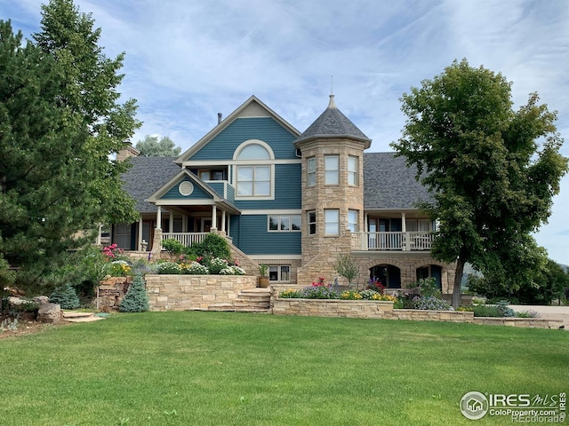 view of front of house featuring a balcony, stone siding, and a front yard