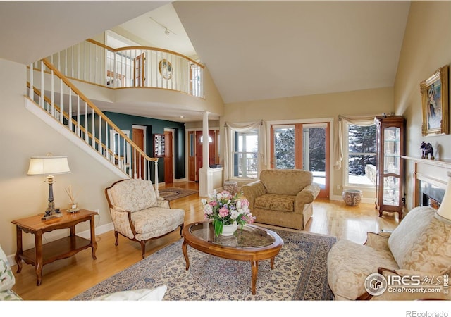 living room with a fireplace, baseboards, stairs, light wood finished floors, and ornate columns