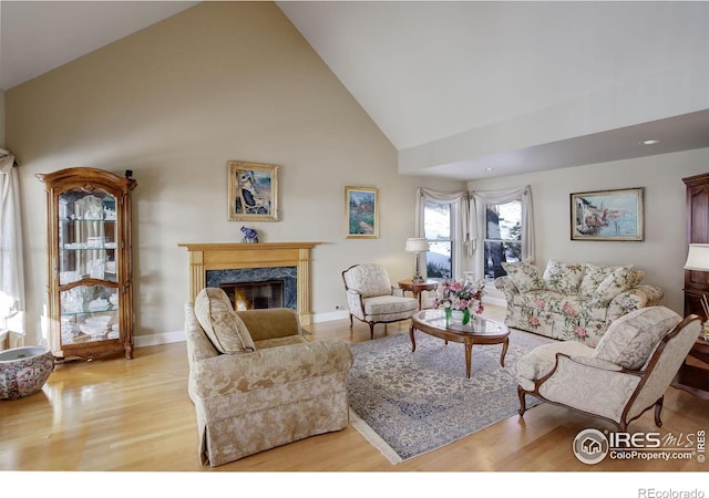 living area with high vaulted ceiling, light wood-style flooring, a high end fireplace, and baseboards