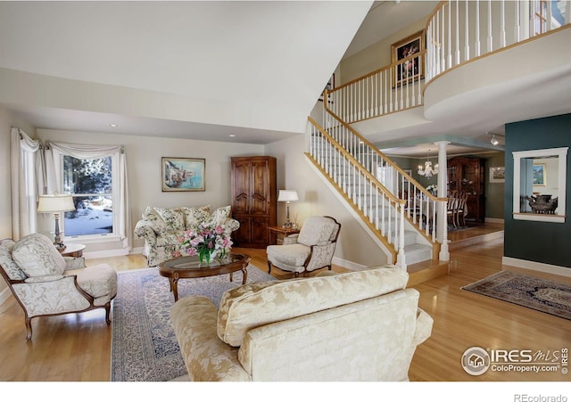 living area with wood finished floors, a towering ceiling, baseboards, stairway, and decorative columns