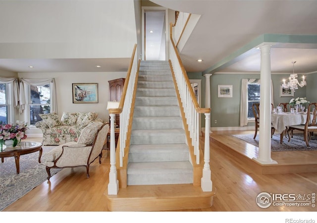 stairway with an inviting chandelier, decorative columns, wood finished floors, and recessed lighting