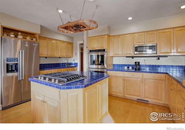 kitchen featuring stainless steel appliances, a center island, visible vents, and light brown cabinetry