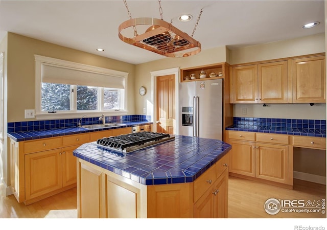 kitchen with a sink, a kitchen island, appliances with stainless steel finishes, tile counters, and light wood finished floors