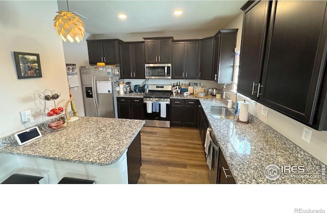 kitchen featuring appliances with stainless steel finishes, wood finished floors, decorative light fixtures, light stone countertops, and recessed lighting