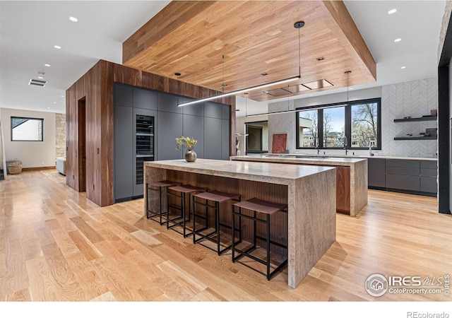 kitchen with hanging light fixtures, a large island, light wood finished floors, modern cabinets, and a kitchen bar