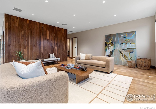 living area with light wood-style floors, recessed lighting, visible vents, and wooden walls