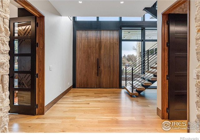 hall with stairs, light wood finished floors, a wall of windows, and baseboards