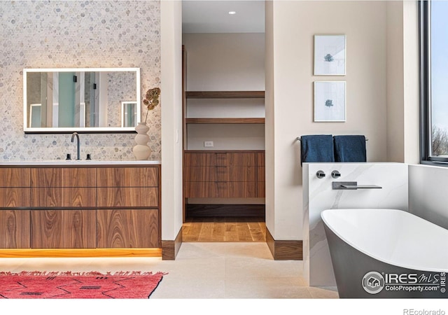 bathroom featuring a soaking tub, vanity, and wallpapered walls