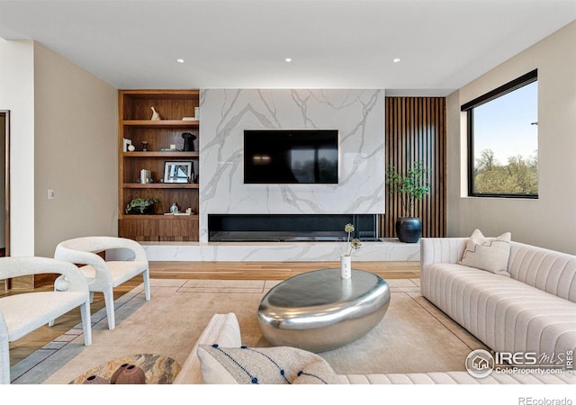 living area featuring built in shelves, an accent wall, a fireplace, and recessed lighting