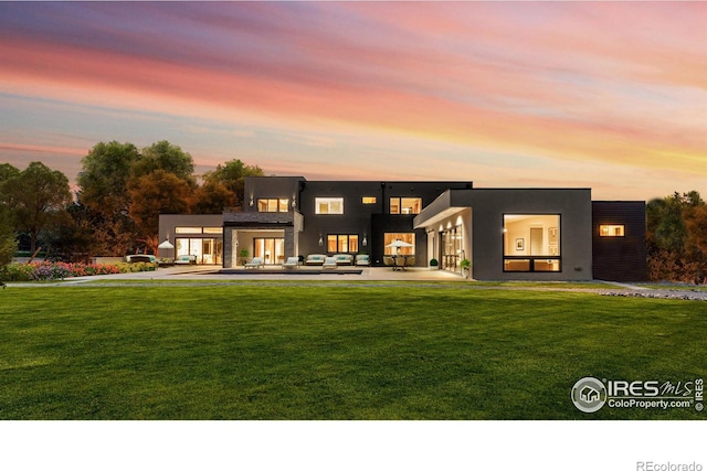 rear view of house featuring a patio area, a lawn, and stucco siding