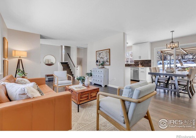 living area featuring baseboards, light wood-style floors, stairway, and a notable chandelier