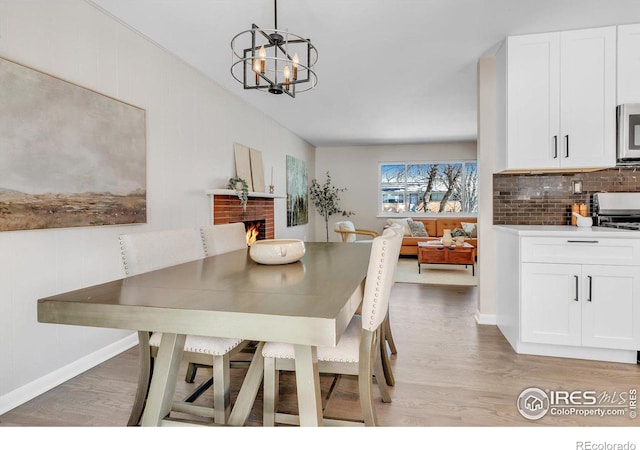 dining space featuring baseboards, a fireplace, light wood finished floors, and an inviting chandelier