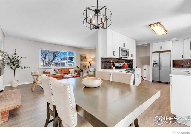 dining area featuring baseboards, light wood finished floors, and an inviting chandelier