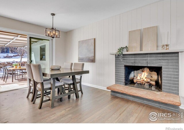 dining space with an inviting chandelier, a lit fireplace, baseboards, and wood finished floors