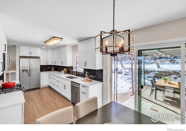 kitchen featuring decorative light fixtures, light countertops, appliances with stainless steel finishes, white cabinetry, and a sink