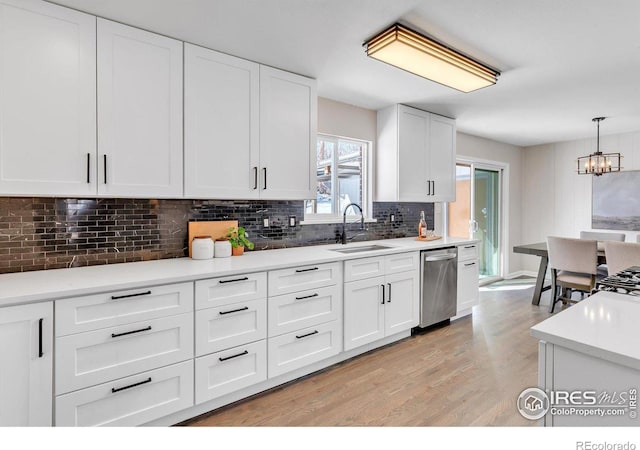 kitchen with hanging light fixtures, a sink, light countertops, white cabinetry, and stainless steel dishwasher