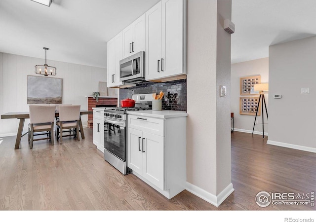 kitchen with hanging light fixtures, light wood-type flooring, appliances with stainless steel finishes, and white cabinets