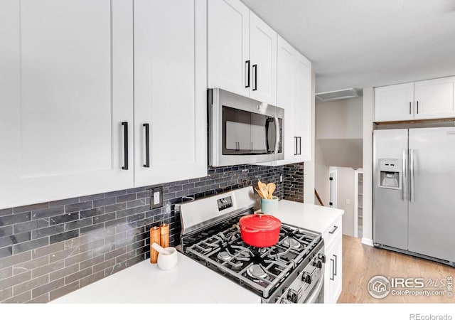 kitchen featuring tasteful backsplash, light countertops, light wood-style flooring, appliances with stainless steel finishes, and white cabinetry