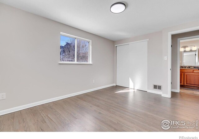 unfurnished bedroom with a closet, visible vents, baseboards, and wood finished floors