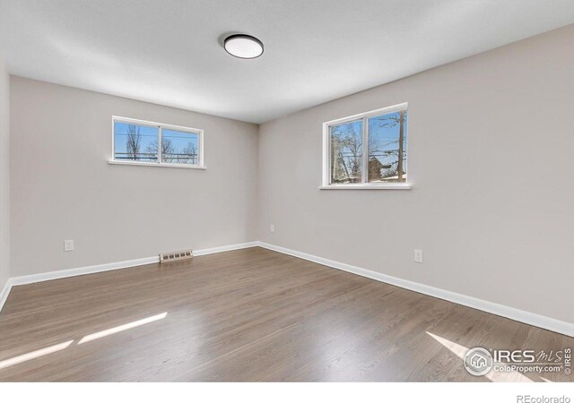 unfurnished room featuring baseboards, wood finished floors, visible vents, and a healthy amount of sunlight