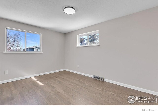 spare room with baseboards, a textured ceiling, visible vents, and wood finished floors