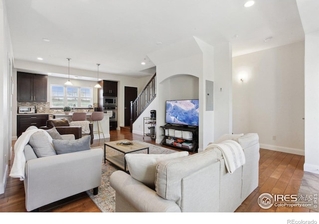 living area featuring recessed lighting, dark wood-style flooring, baseboards, and stairs