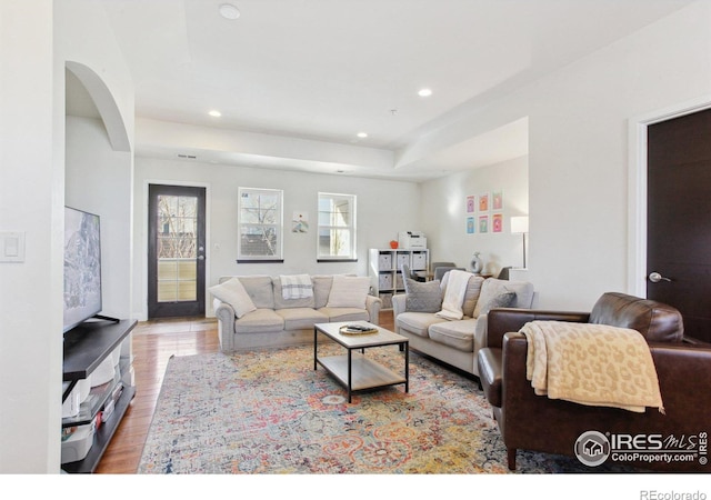 living room featuring light wood-style floors, a raised ceiling, and recessed lighting