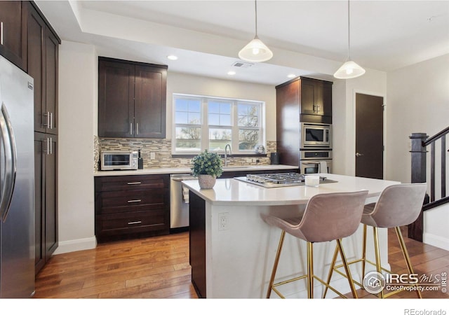 kitchen featuring decorative backsplash, a kitchen island, appliances with stainless steel finishes, dark wood-type flooring, and light countertops