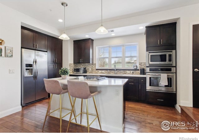 kitchen featuring stainless steel appliances, a kitchen island, dark brown cabinets, light countertops, and backsplash