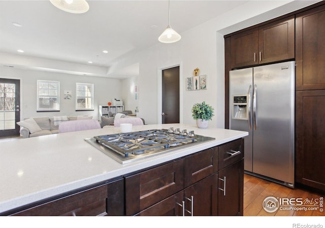 kitchen featuring decorative light fixtures, light wood finished floors, light countertops, appliances with stainless steel finishes, and open floor plan