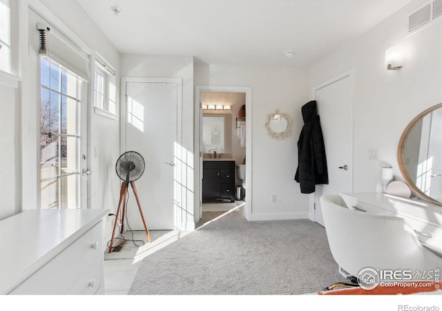 interior space featuring ensuite bath, visible vents, baseboards, and light colored carpet