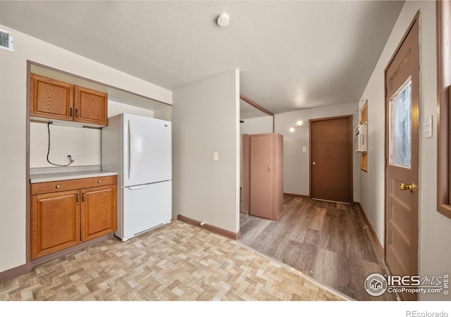 kitchen with brown cabinets, parquet floors, light countertops, and freestanding refrigerator