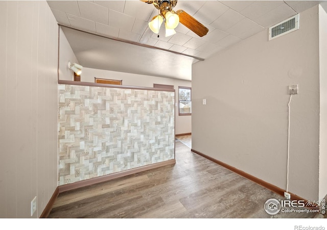 empty room featuring a ceiling fan, baseboards, visible vents, and wood finished floors