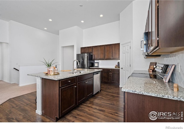 kitchen featuring dark wood finished floors, light stone counters, a kitchen island with sink, stainless steel appliances, and a sink