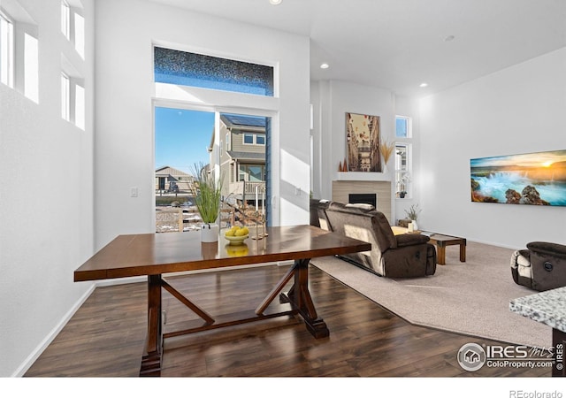 living area featuring recessed lighting, a fireplace, a towering ceiling, baseboards, and dark wood-style floors